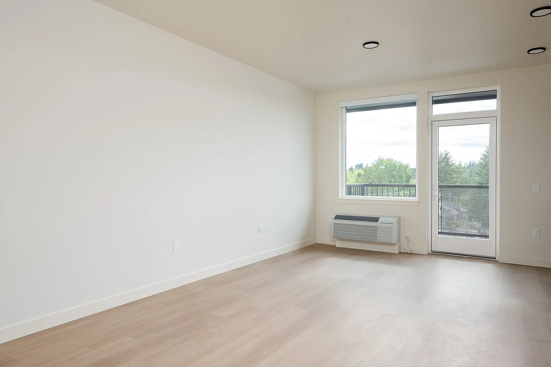 Empty apartment living room with large window and balcony door.