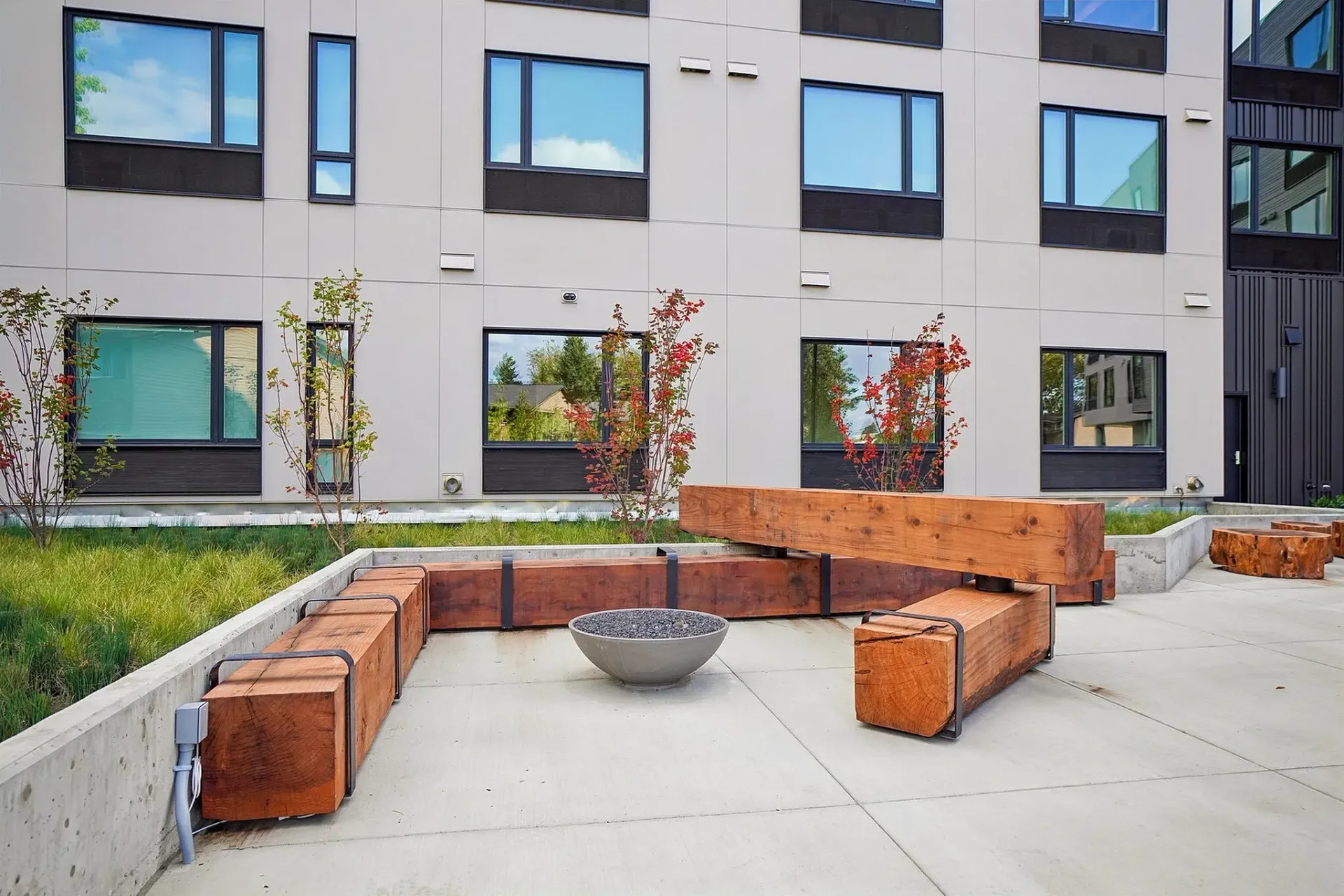 Outdoor seating area with wooden benches and a fire pit in front of a modern building.