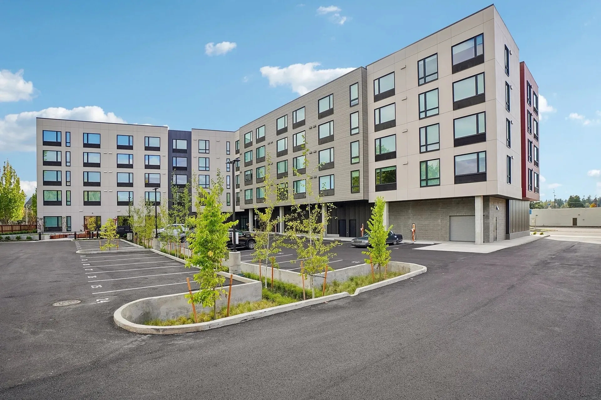 Exterior of a modern apartment building with a large parking lot.