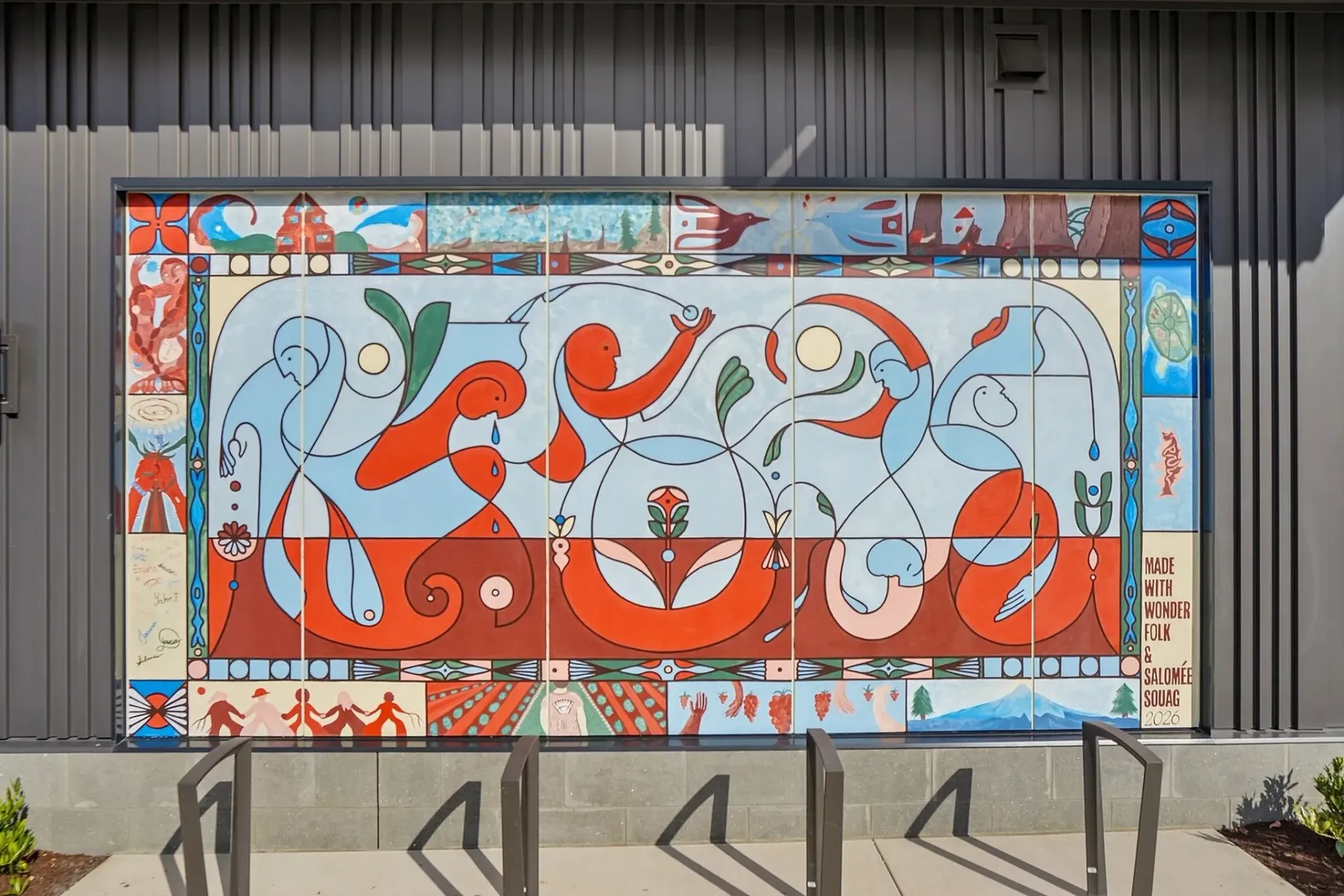 Mural on the side of a building featuring abstract figures, nature elements, and text that says 