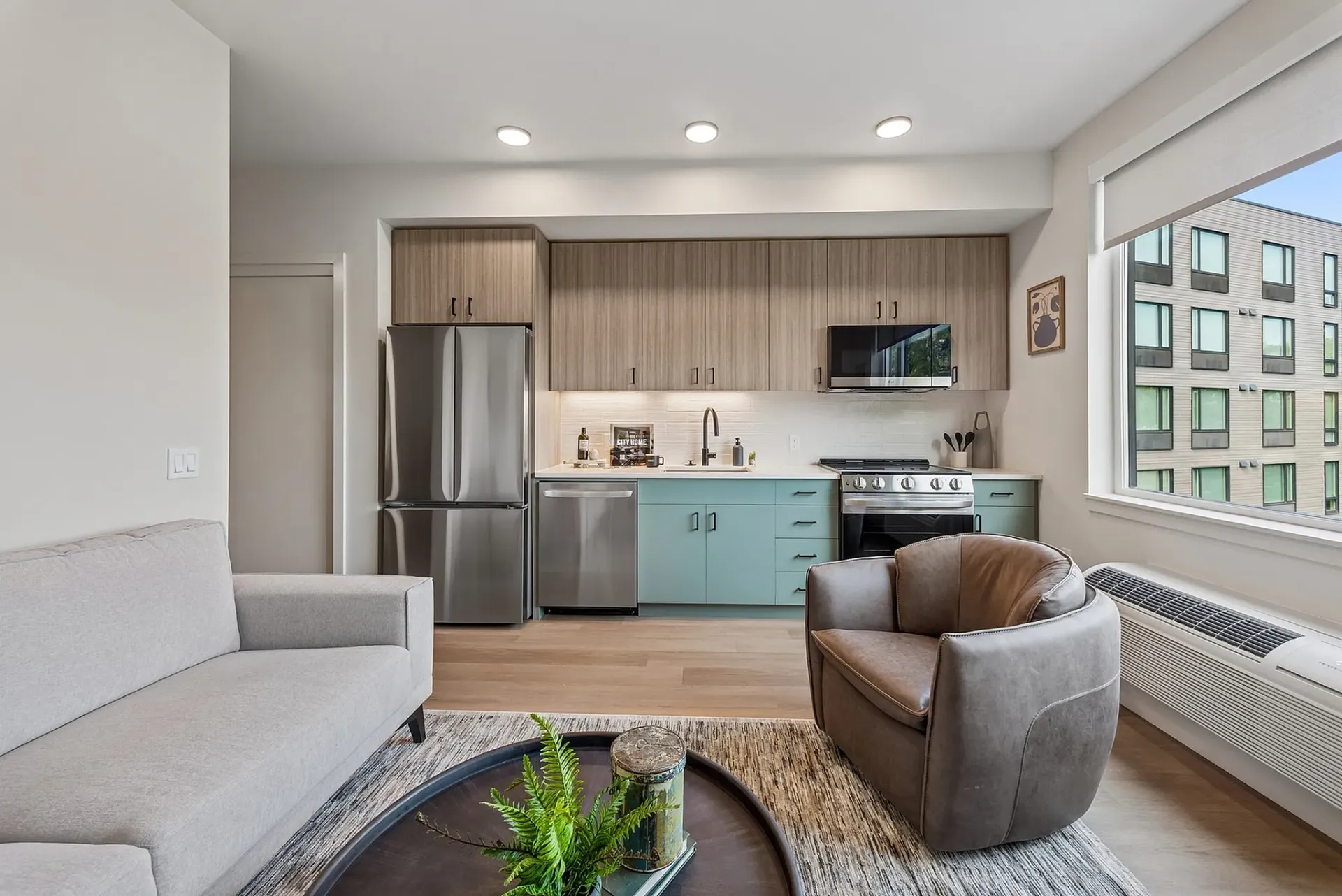 Modern apartment kitchen with stainless steel appliances, light wood cabinets, and teal lower cabinets.