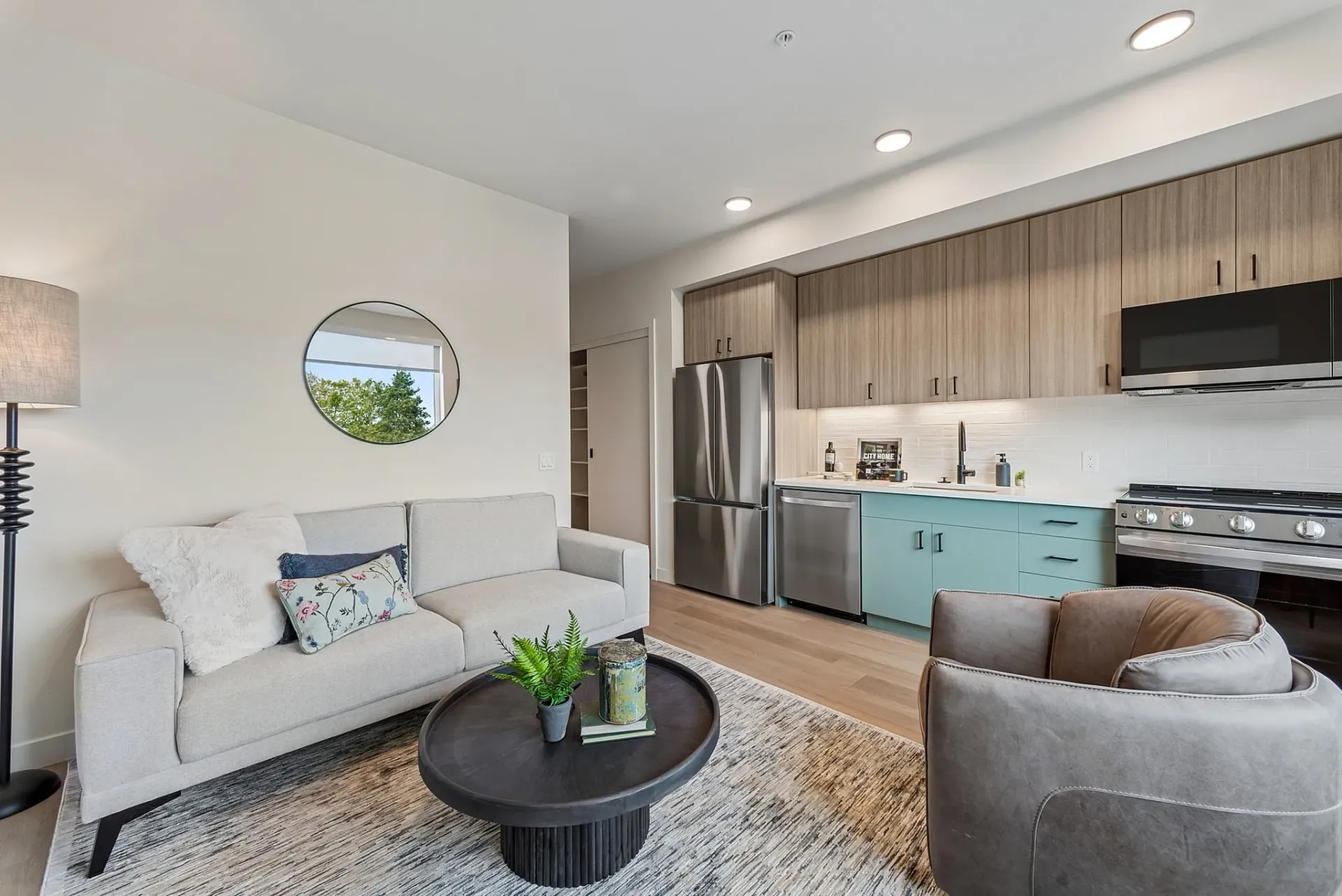 Modern living room with open-concept kitchen featuring a sofa, coffee table, and stainless steel appliances.