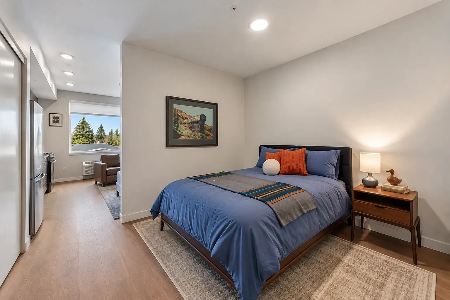 Modern bedroom with blue bedding, orange accent pillows, and a wooden nightstand with a lamp.