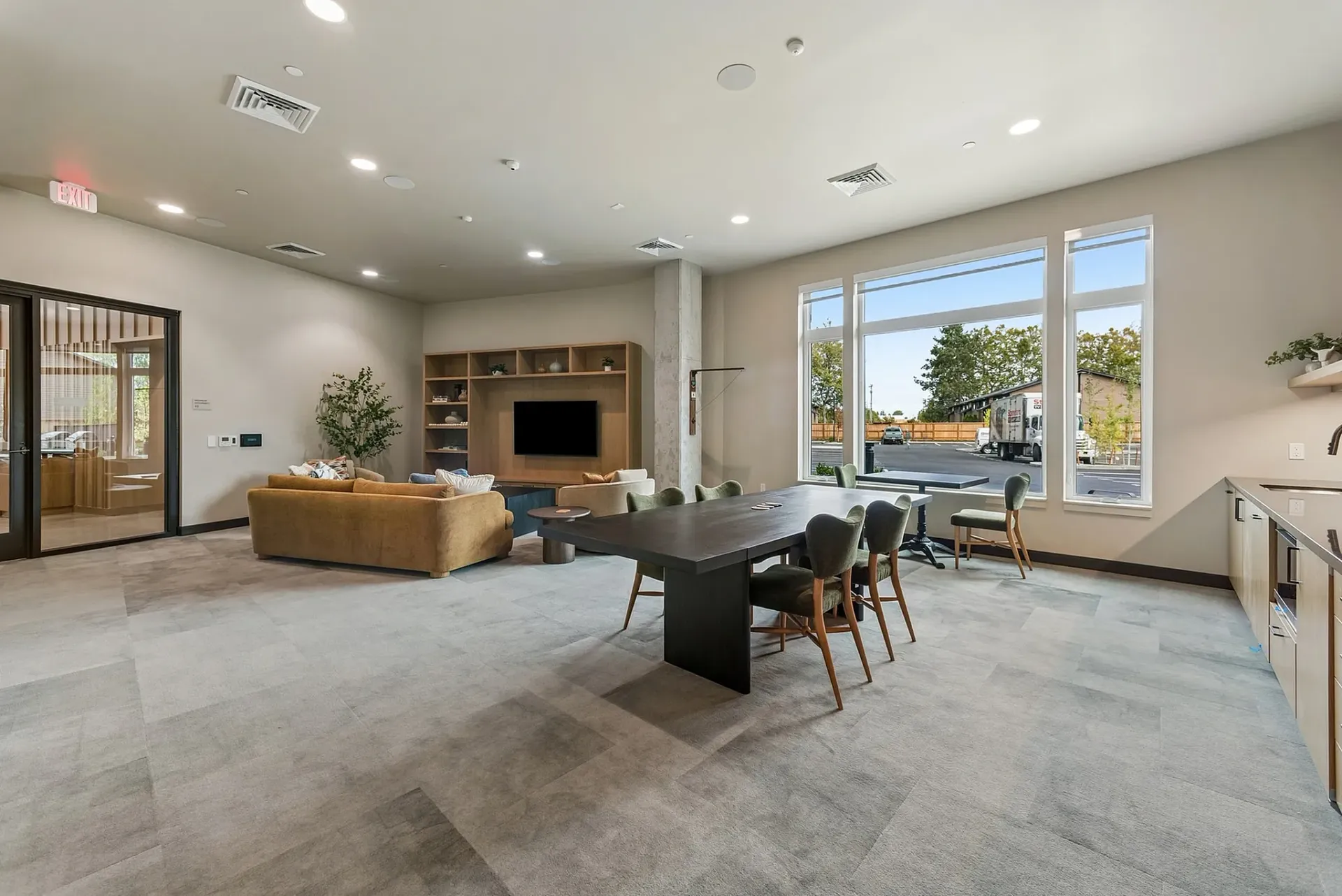 Community lounge area with large windows, a dining table, sofas, and a TV.