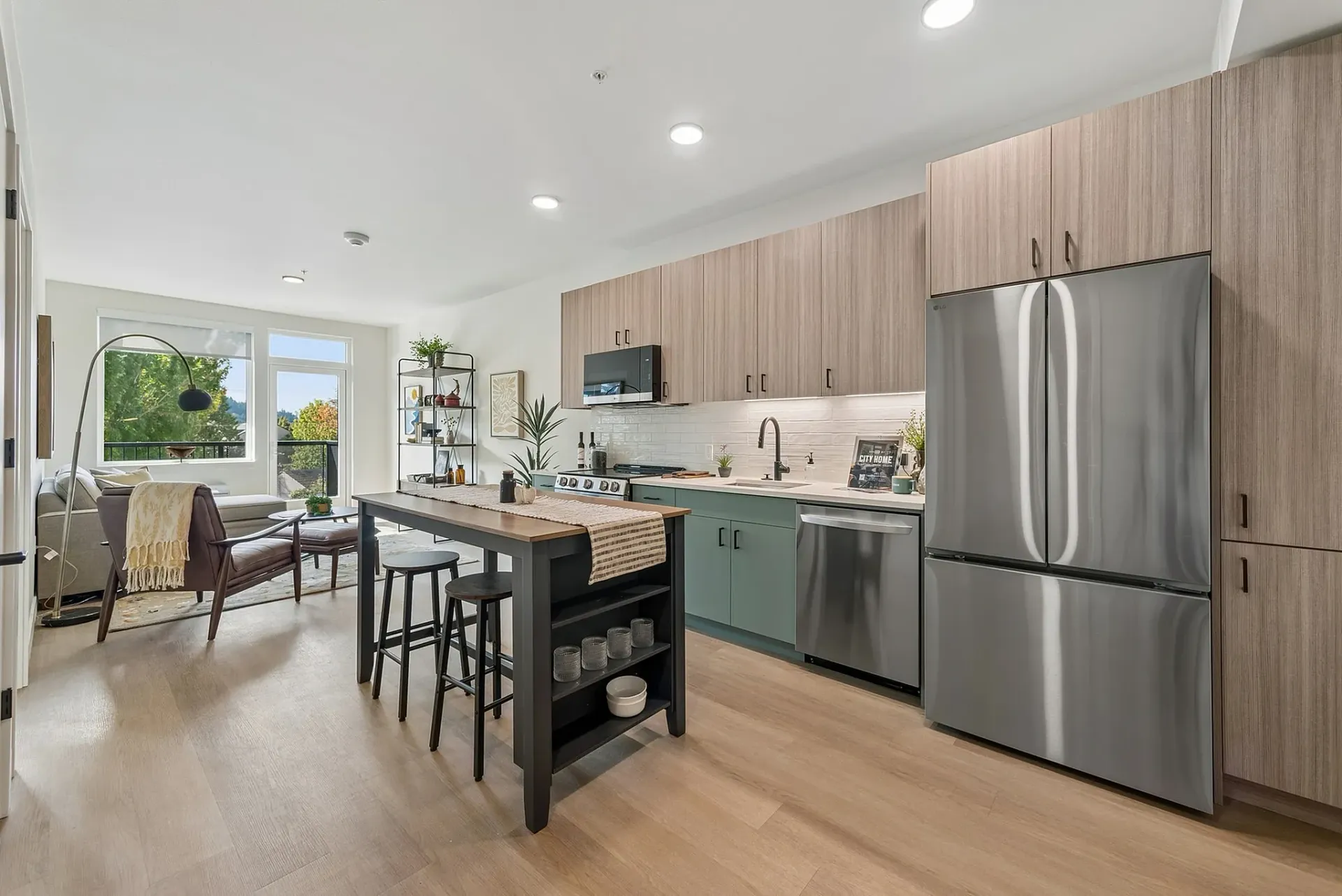 Modern kitchen and living area with island seating, stainless steel appliances, and large windows.