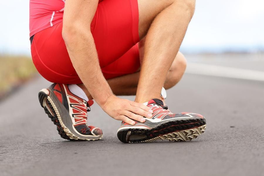 Runner, crouched on pavement, touching his ankle; wearing red athletic gear and running shoes.