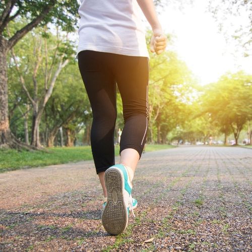 Person walking on a path in a sunny park; wearing leggings and sneakers.