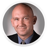 Bald man in a suit smiling, head and shoulders portrait.
