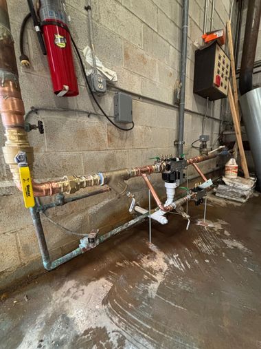 Utility pipes and valves against a concrete wall, with water leaking onto the floor.