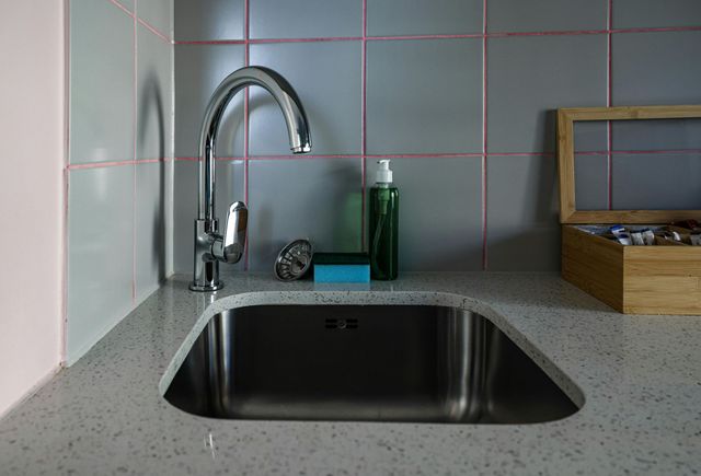 Kitchen sink with chrome faucet, gray countertop, tiled backsplash, and dish soap bottle nearby