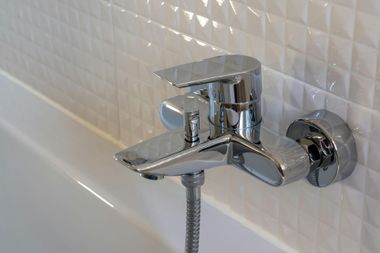 Chrome bathtub faucet with handheld shower hose against white tile wall
