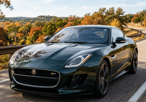 Dark green Jaguar F-Type driving along a winding road surrounded by colorful fall foliage