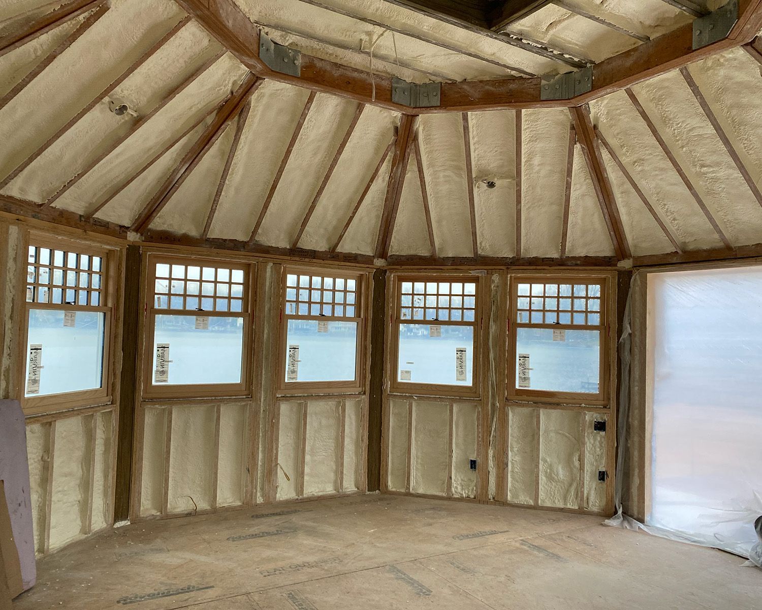 An unfinished room under construction, featuring exposed wooden beams, insulation-filled walls, and a concrete floor.