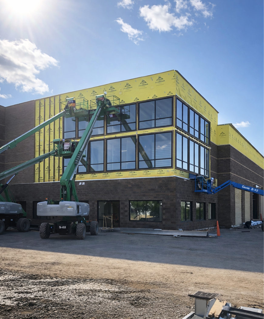 A gloved hand touches blue sound-insulating material installed between metal wall studs in an office construction site.
