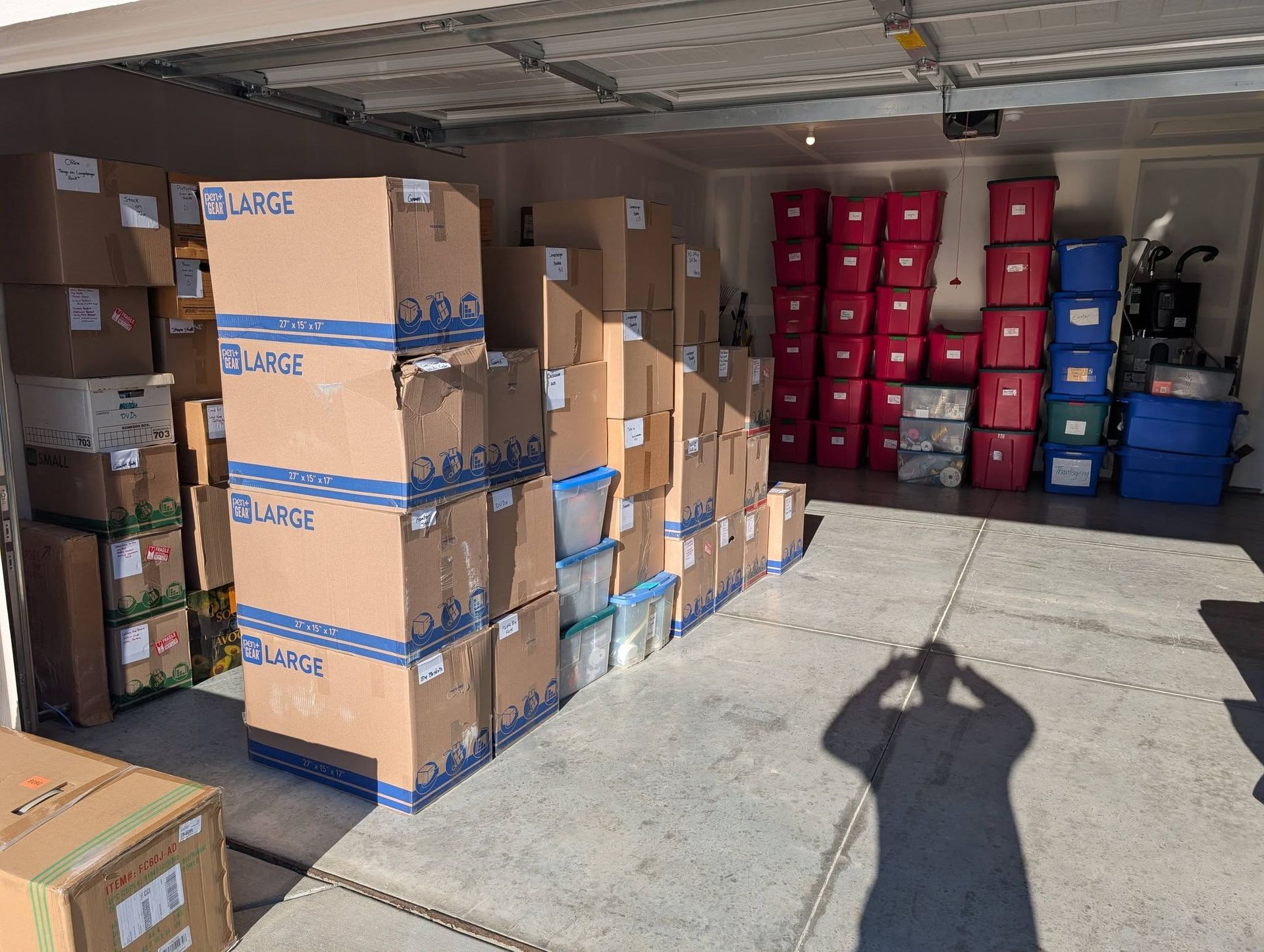 Warehouse garage with stacked cardboard boxes and blue storage bins in a bright loading area.