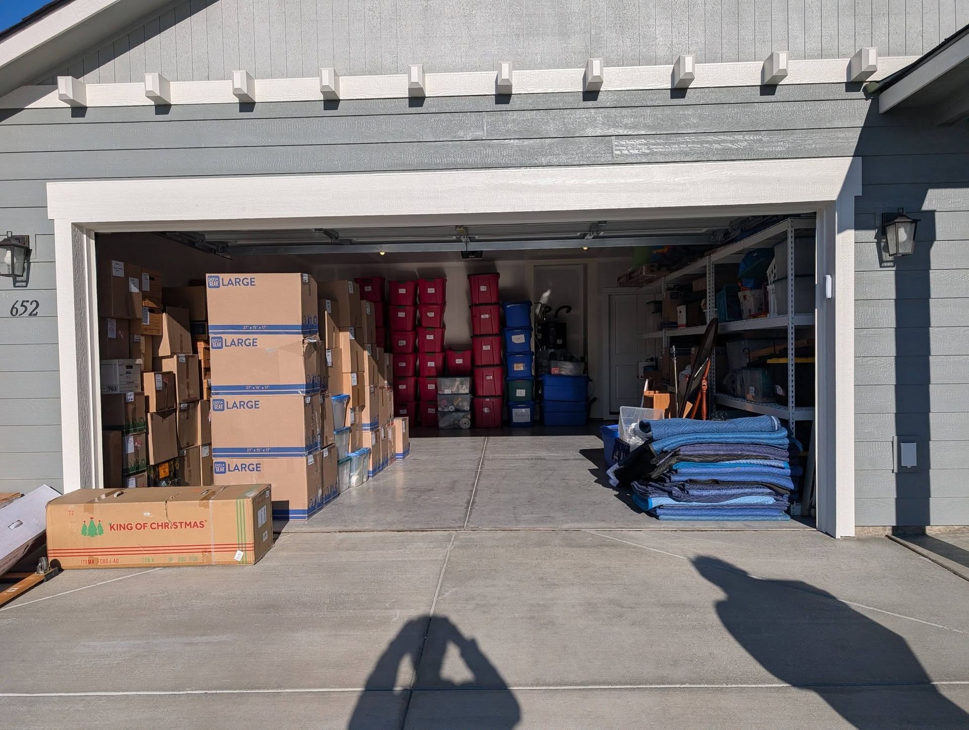 Open garage packed with stacked boxes, red cylinders, and blue pallets in a storage area.