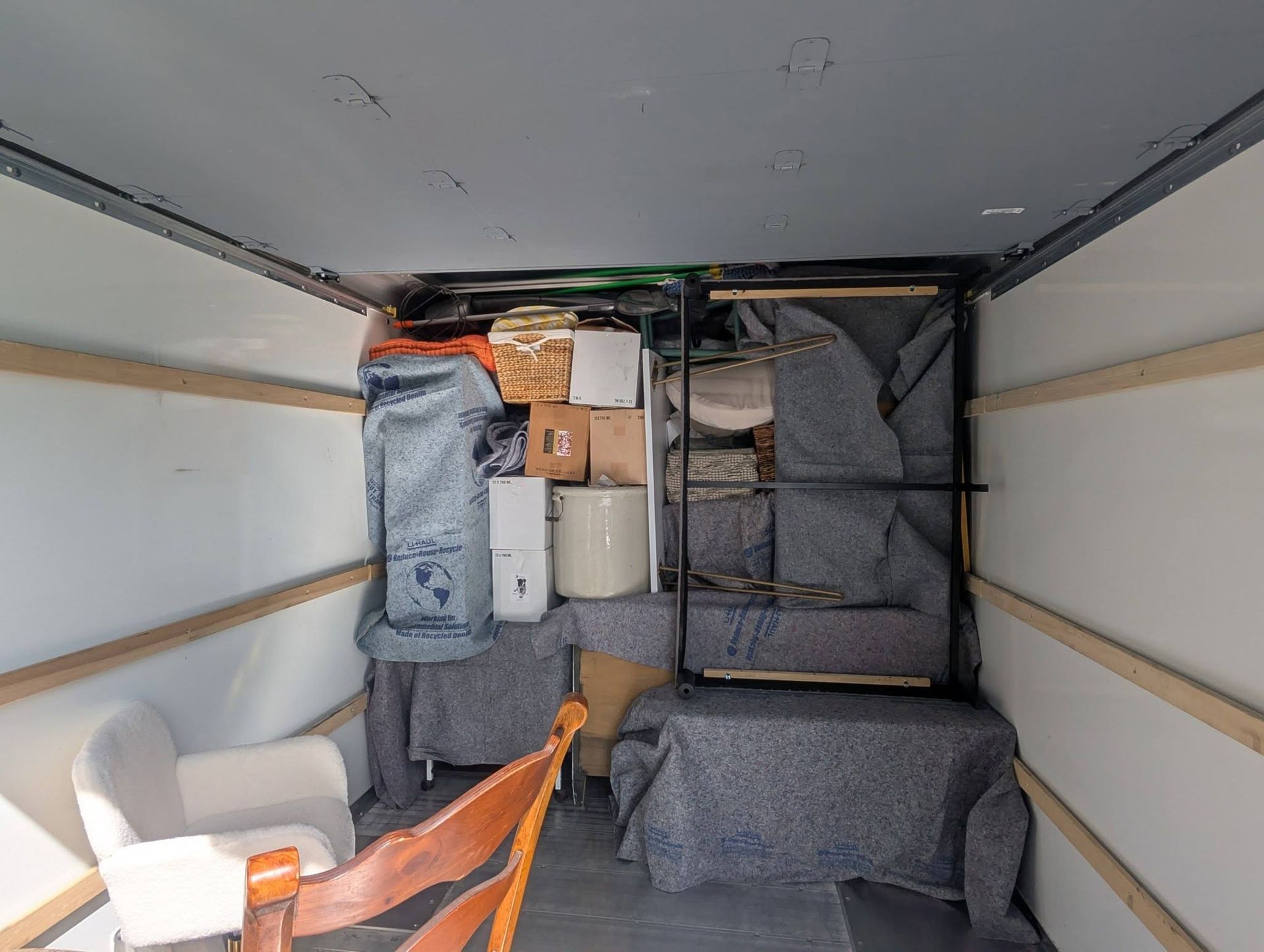 Inside a truck trailer, gray padded packing panels secure stacked boxes and furniture