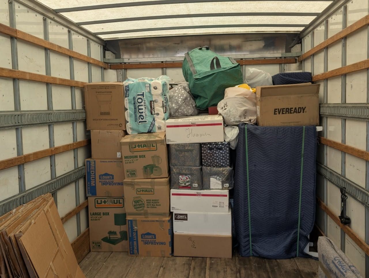 Packed moving truck with stacked boxes, bags, and furniture inside a white cargo trailer.
