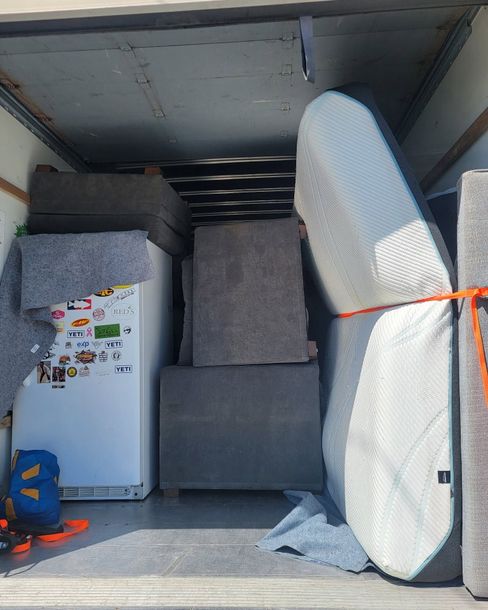 Packed moving truck with a refrigerator, mattress, and furniture strapped inside.