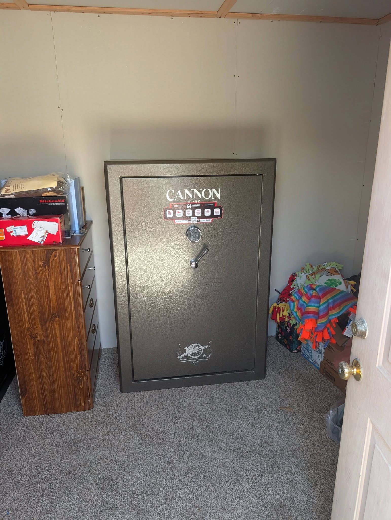 Small room with a large metal safe against the wall, a cabinet on the left, and a pile of colorful items on the right.