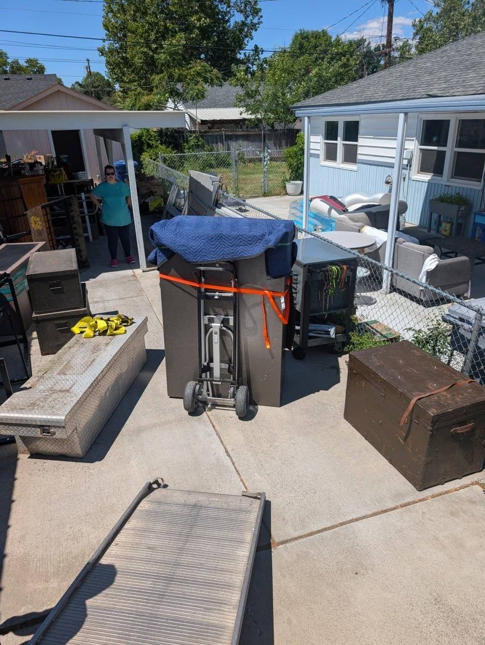 Backyard patio with a large covered trash bin, outdoor furniture, and a shed in the background.