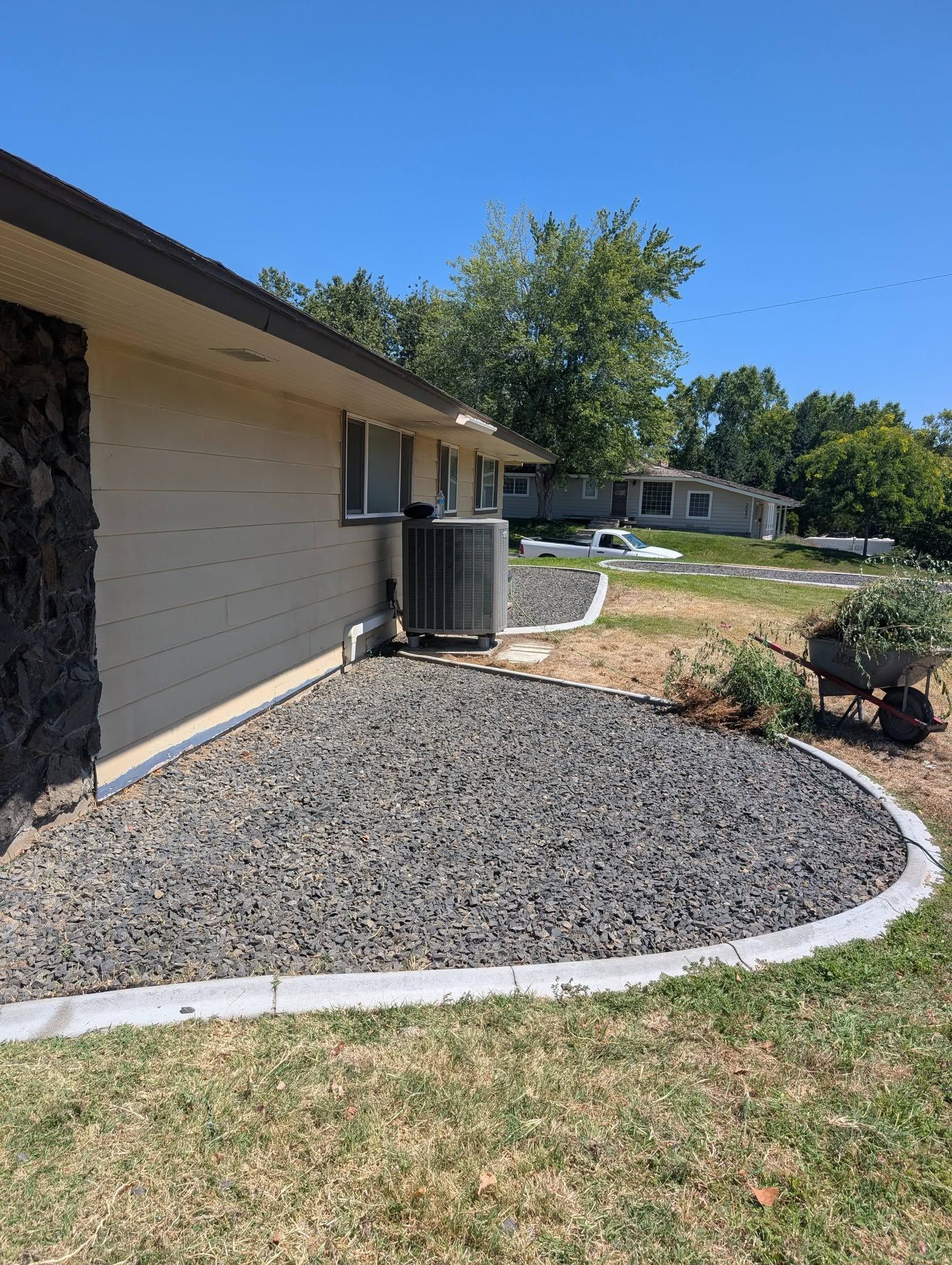 House exterior with beige siding, dark gravel landscaping, and curved white edging under a clear blue sky