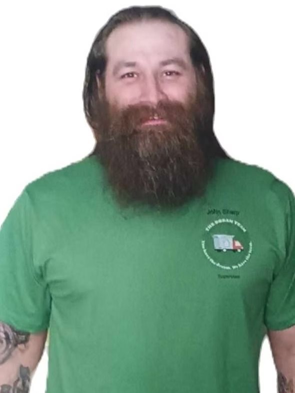 Man in green T-shirt with long beard, standing against a white background.