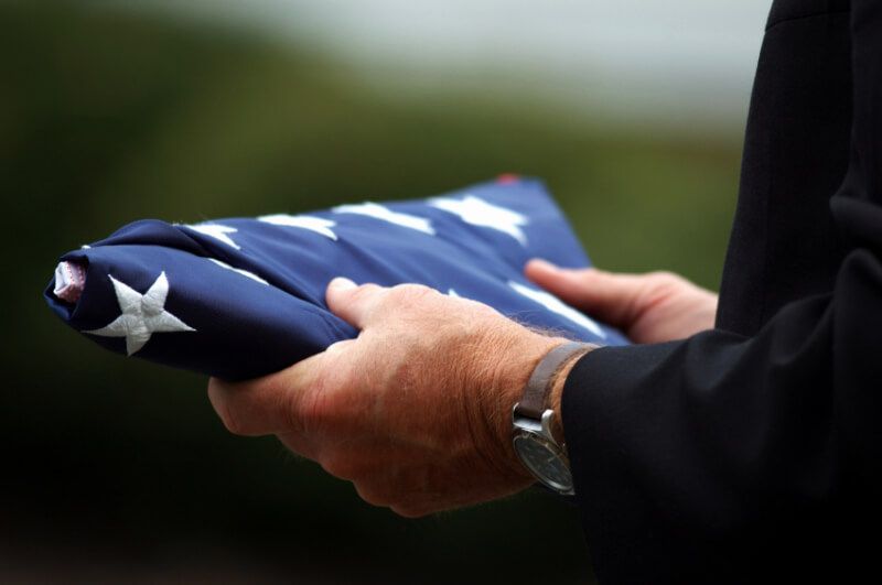 Hands folding a folded American flag with white stars on blue fabric outdoors.