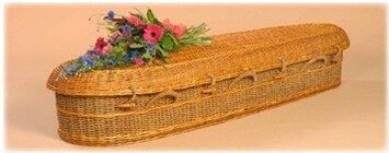 Wicker casket with lid and floral arrangement on top, shown against a plain beige background
