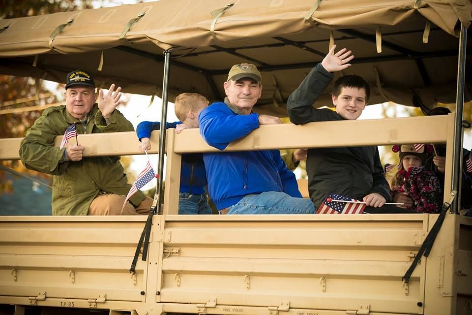 People waving from a tan open vehicle with canvas roof, smiling behind a wooden railing