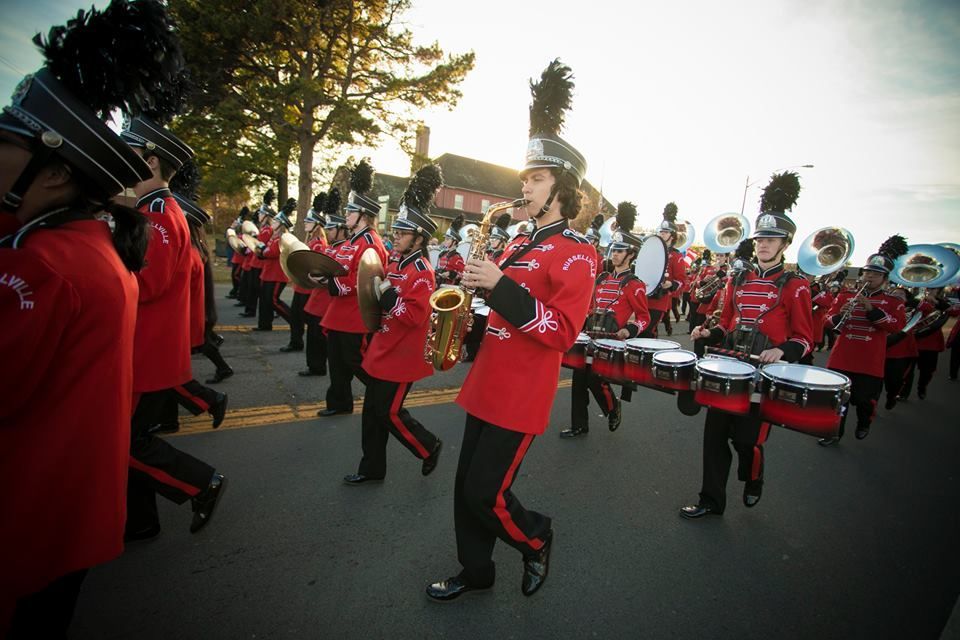 Marching band in red uniforms performing outdoors on a street during daylight