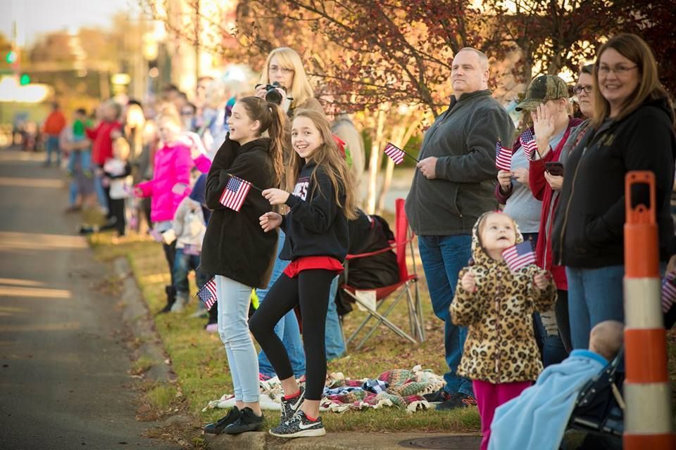 People lining a sidewalk, clapping and watching a parade, with children and a traffic cone nearby