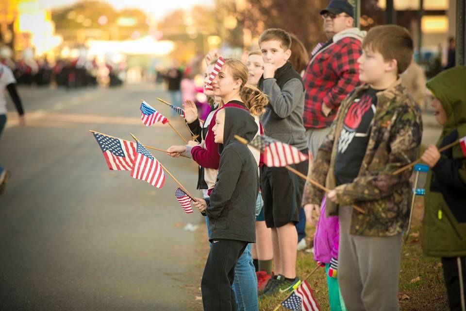 Children and adults holding small American flags at a street-side gathering at dusk