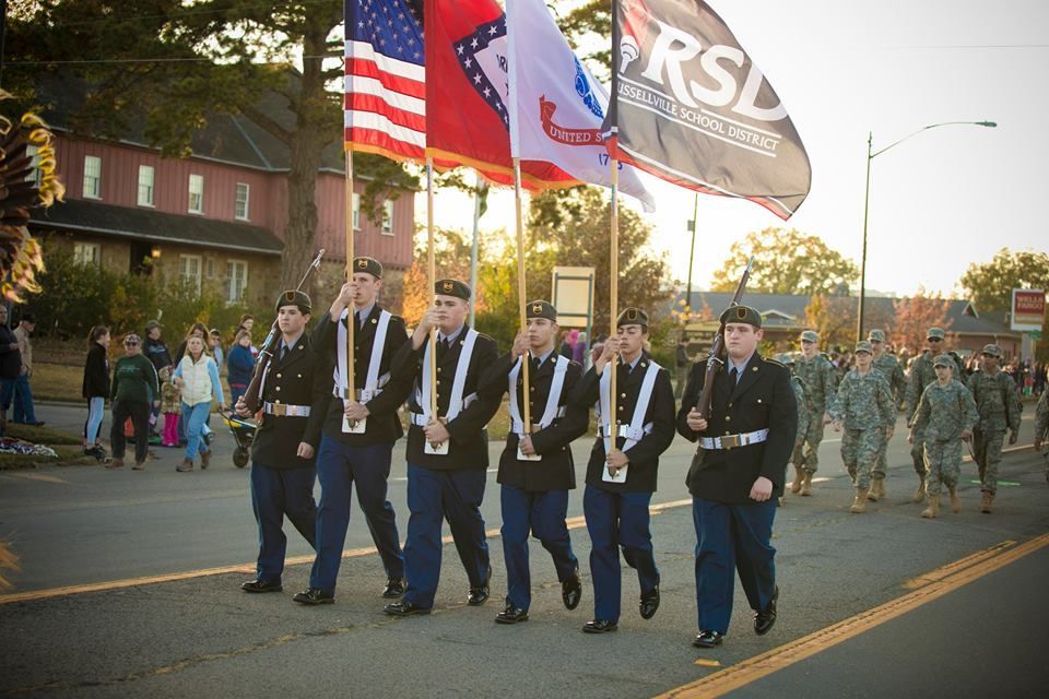 ROTC cadets marching in uniform with flags during a parade at sunset