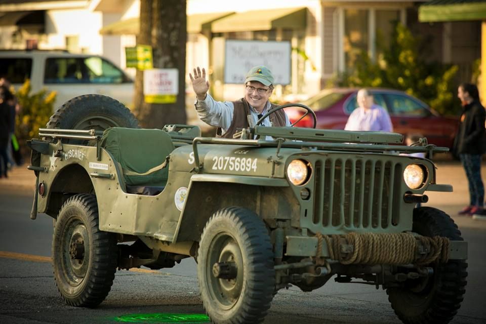 Vintage green military jeep with a waving driver on a street at sunset
