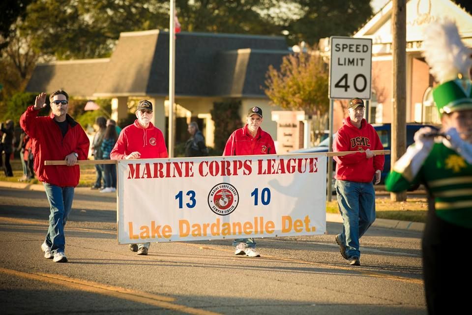 People holding a Marine Corps League banner during a street parade, with a speed limit sign in the background