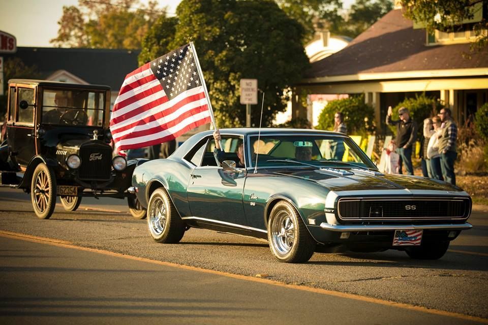 Green classic convertible with American flag in a parade on a sunlit street