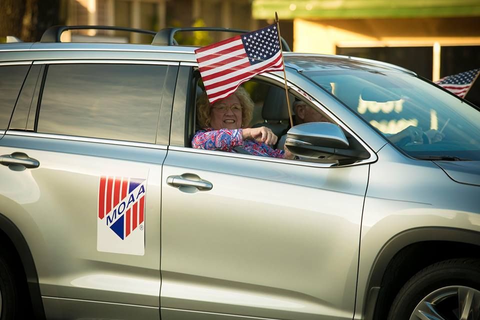 Silver SUV with a U.S. flag and campaign-style signs on the doors, driver visible through the window