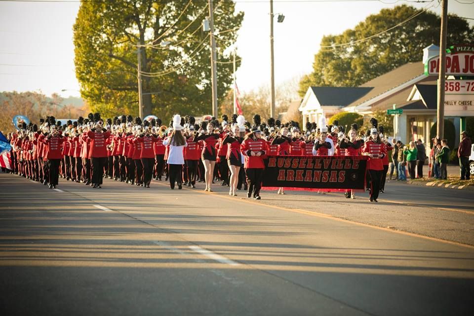 Parade marchers in red shirts carry banners down a sunlit street