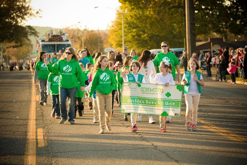 People in green shirts walking in a community march holding signs on a tree-lined street