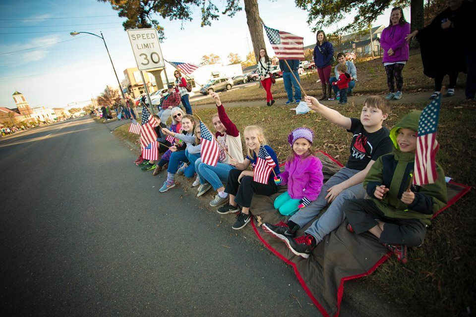 Children waving small American flags while sitting on a sidewalk at a roadside parade