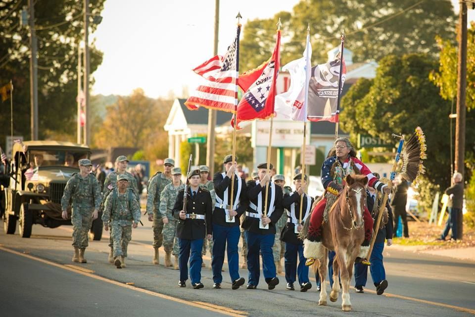 Uniformed parade group marching with flags and horseback riders on a sunlit street