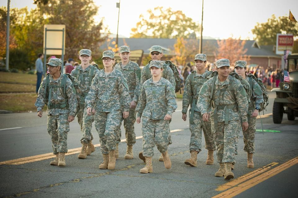 Camouflaged soldiers marching in formation on a sunlit street at sunset