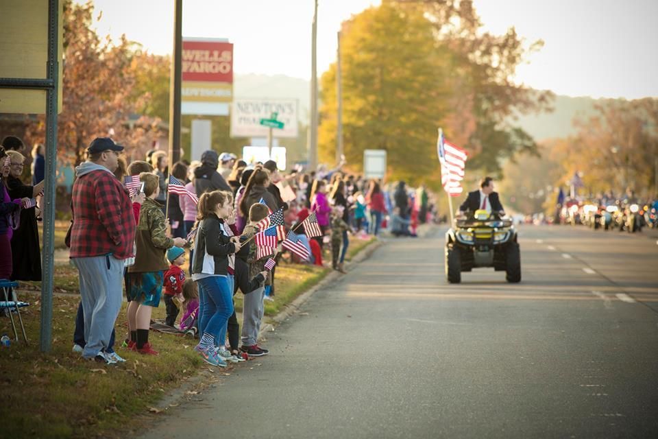 Crowd lining a street watches a person on an ATV during a parade at sunset