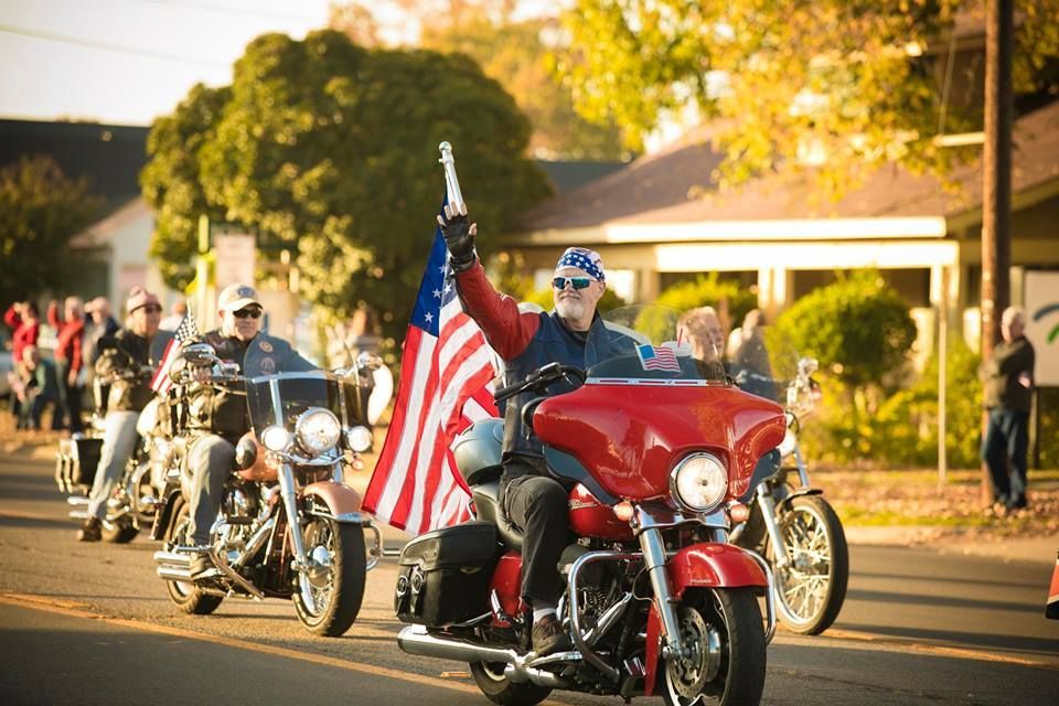 Motorcyclists in a parade with an American flag, riding down a sunlit street