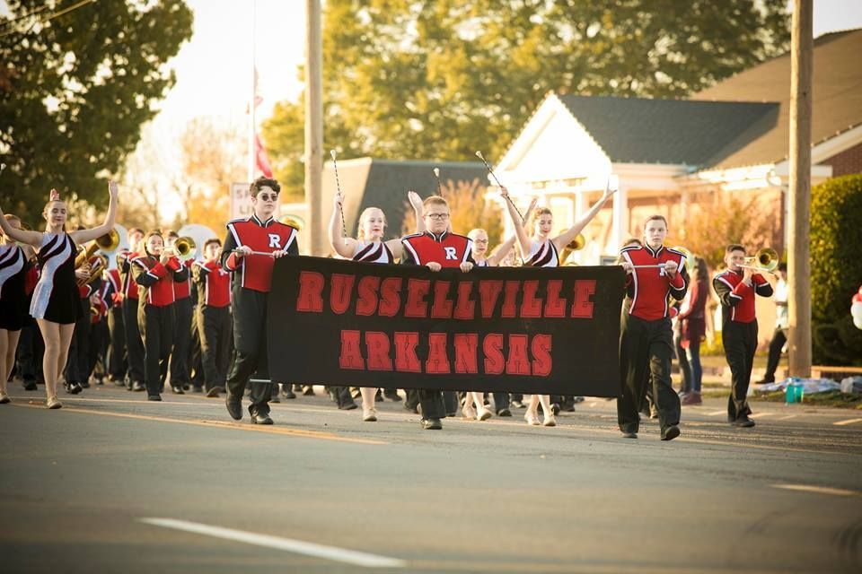 Marching band carrying a black banner reading “Russellville Arkansas” down a street