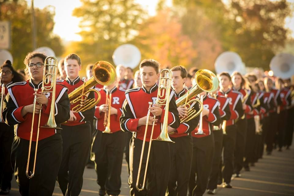 High school marching band in red uniforms performing outdoors in a parade line