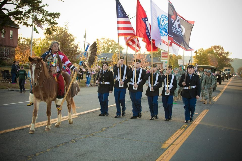 Color guard marching with flags and a mounted rider in a street parade at sunset