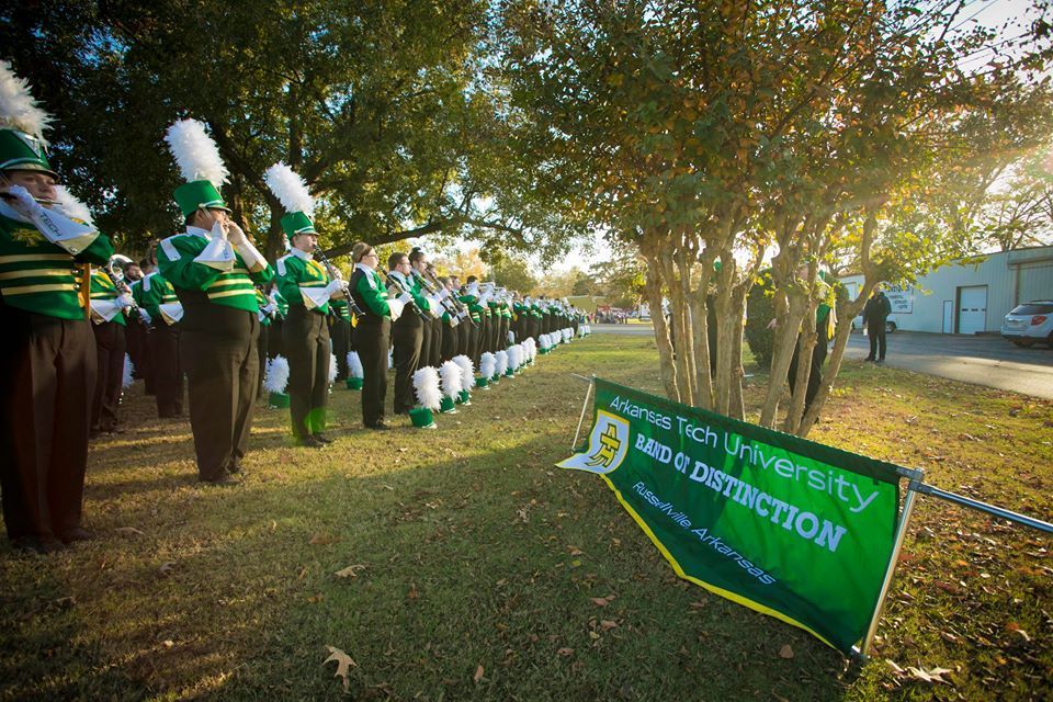Green University of Zimbabwe banner beside a marching band lined up on a sunny lawn.
