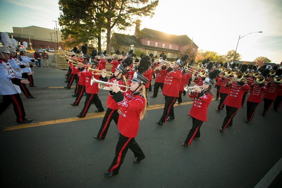 Marching band in red uniforms performing outdoors on a sunny street during a parade